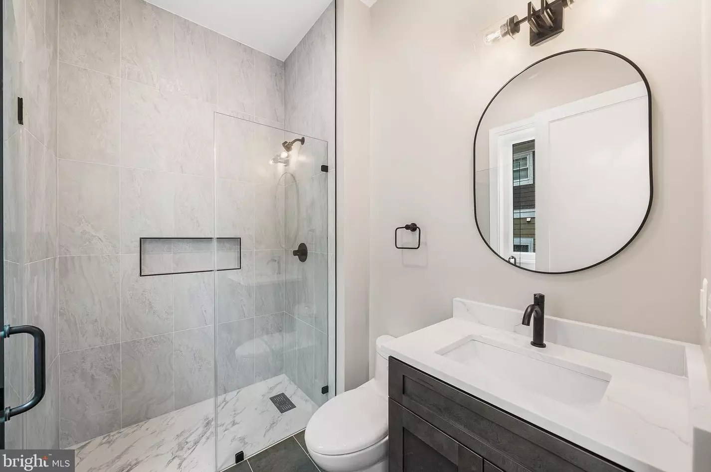 Primary bath with dual-sink vanity, glass shower and round mirror