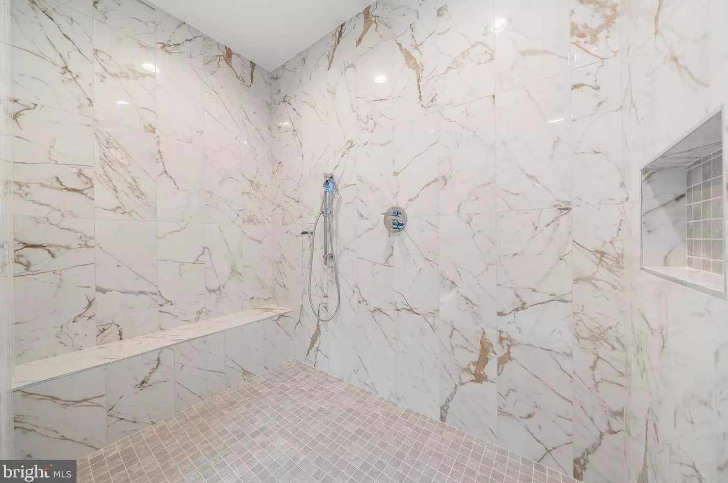 Oversized primary shower with book-matched marble-look tile and bench
